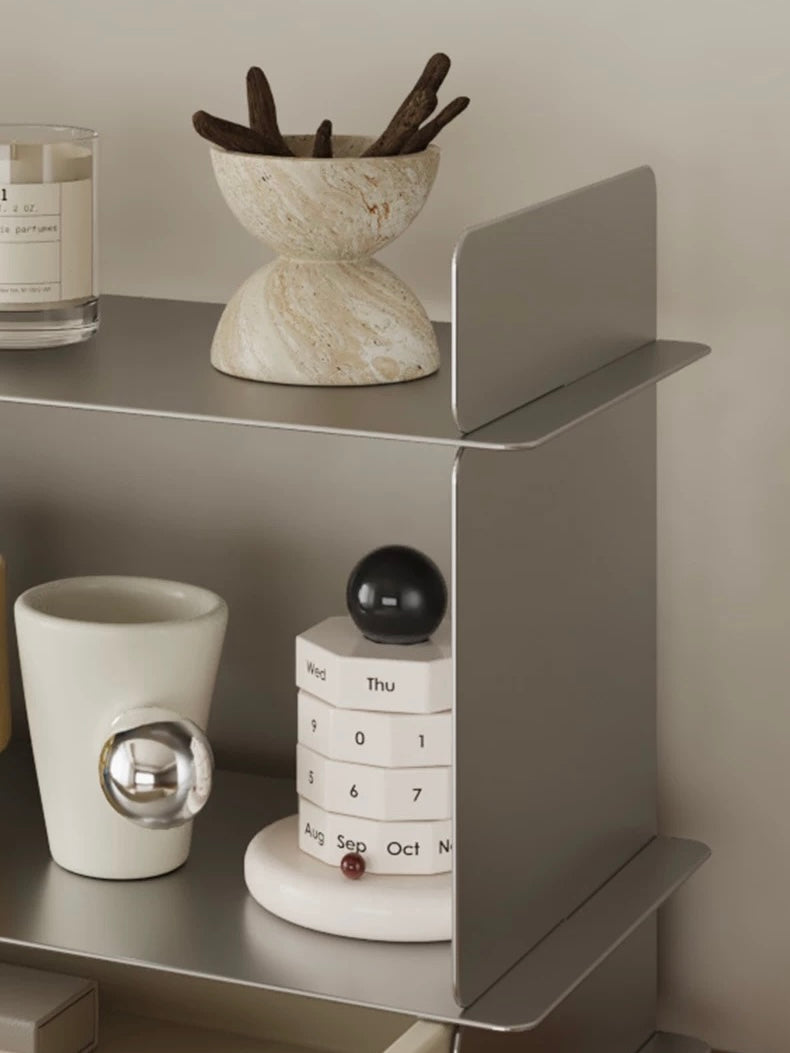 Close up of the top level of the stainless steel shelf with a stone bowl, a flip calendar and a mug with a silver ball handle