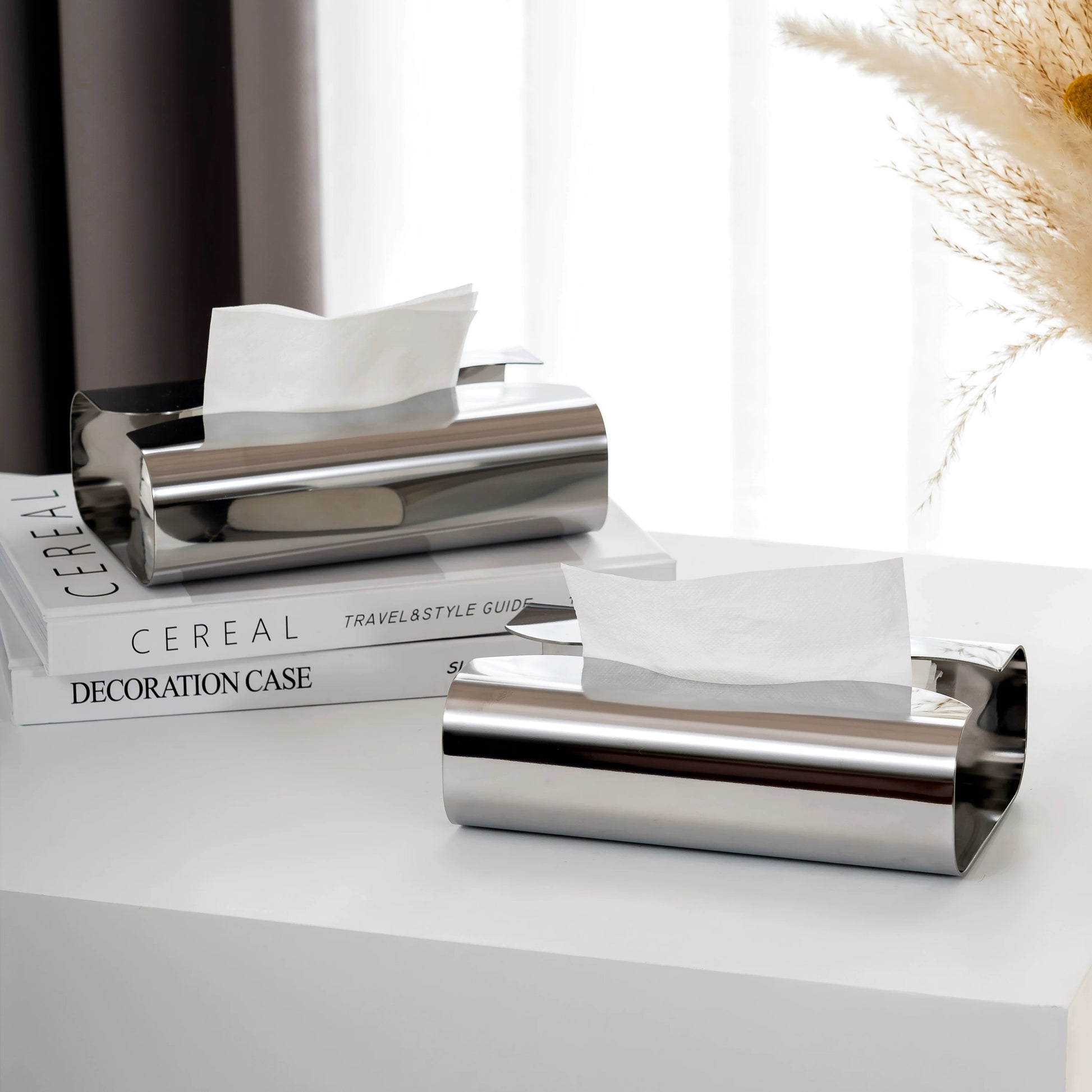 Silver tissue paper holder on a white surface with books in the background
