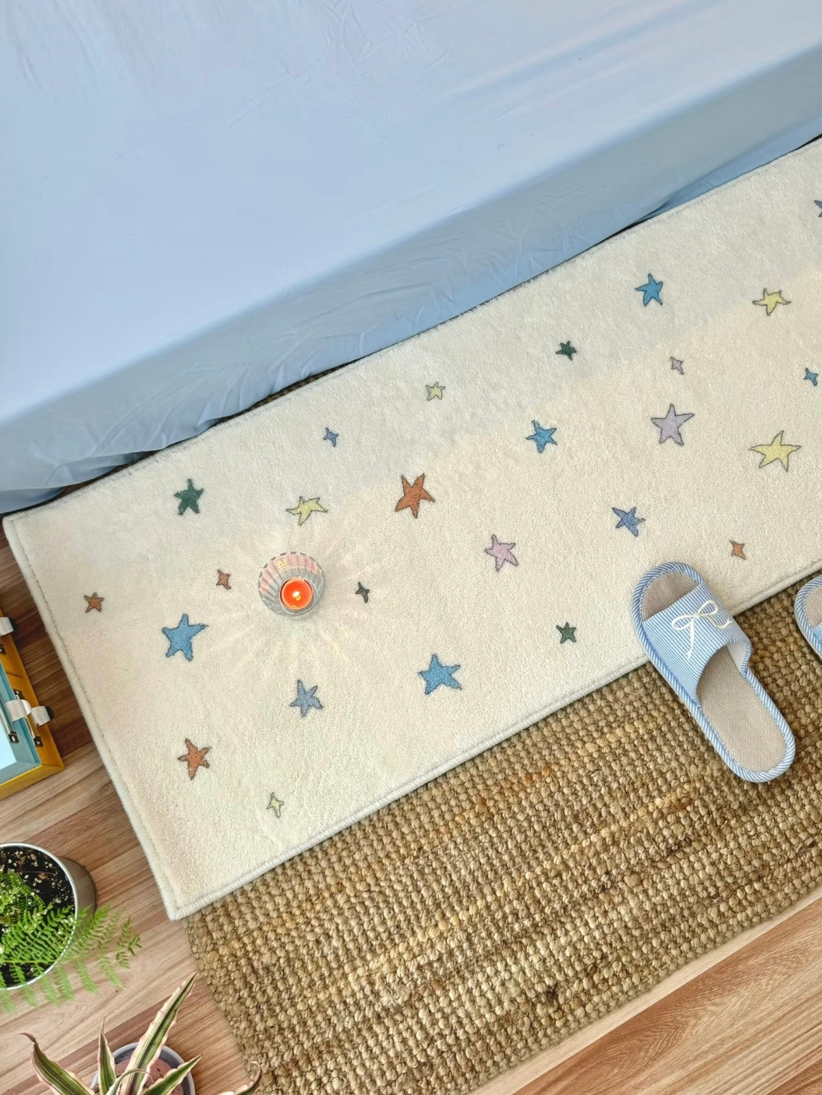 A cream star area rug with multicolor motifs sits beside a blue bed, viewed from a higher angle.