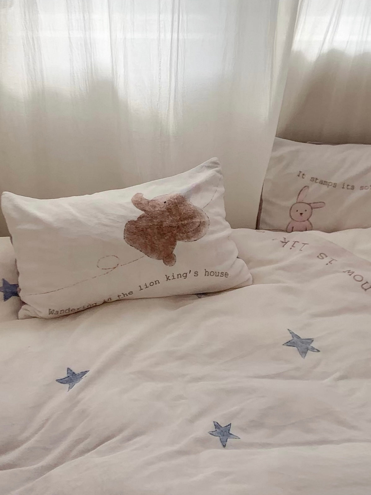 Blue stars spread across the cream cover below an elephant pillowcase by the curtain.