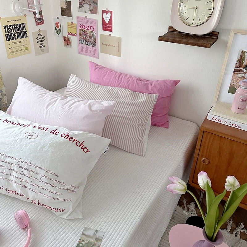 Bedroom with pink and white pillows, a clock, and decorative items on the wall.