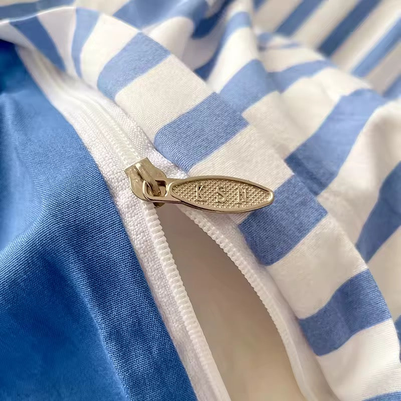 Blue striped bedding with matching pillowcases shown with plush bear and headphones.