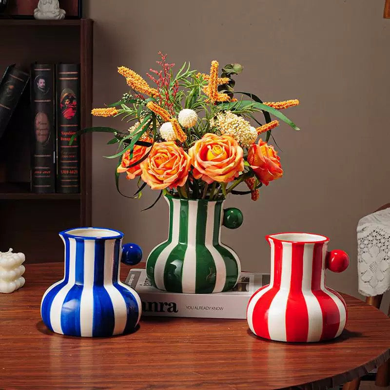 Three colorful vases on a wooden table with a bouquet of flowers in the center.