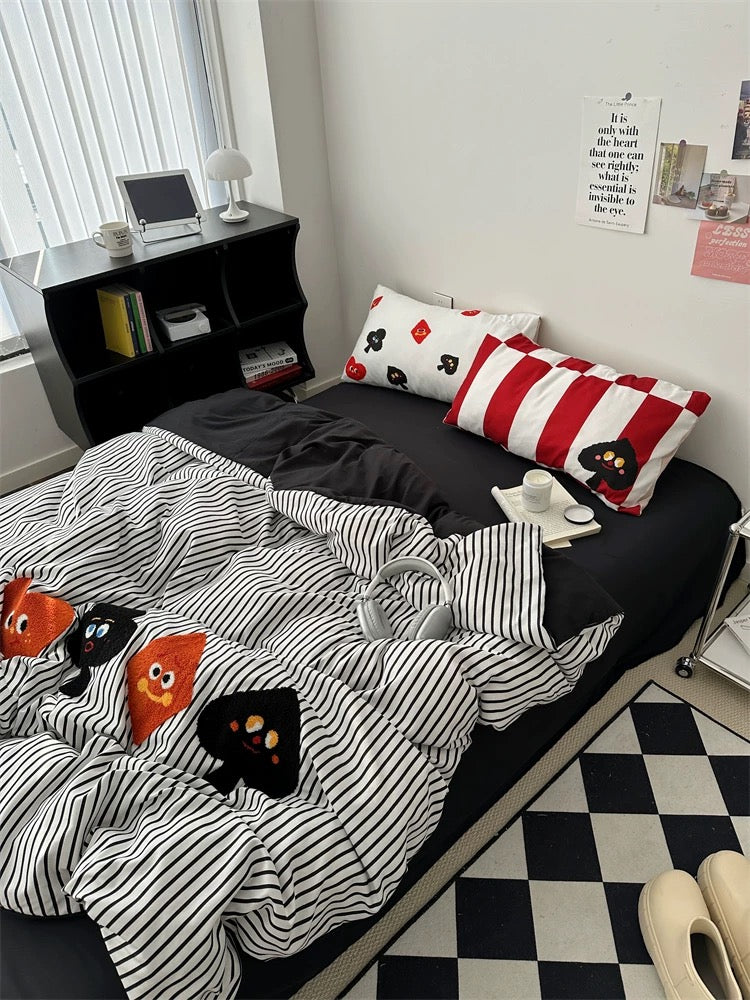 Bed with black and white striped bedding featuring cartoon characters, red and white striped pillows, and a small table with a laptop.
