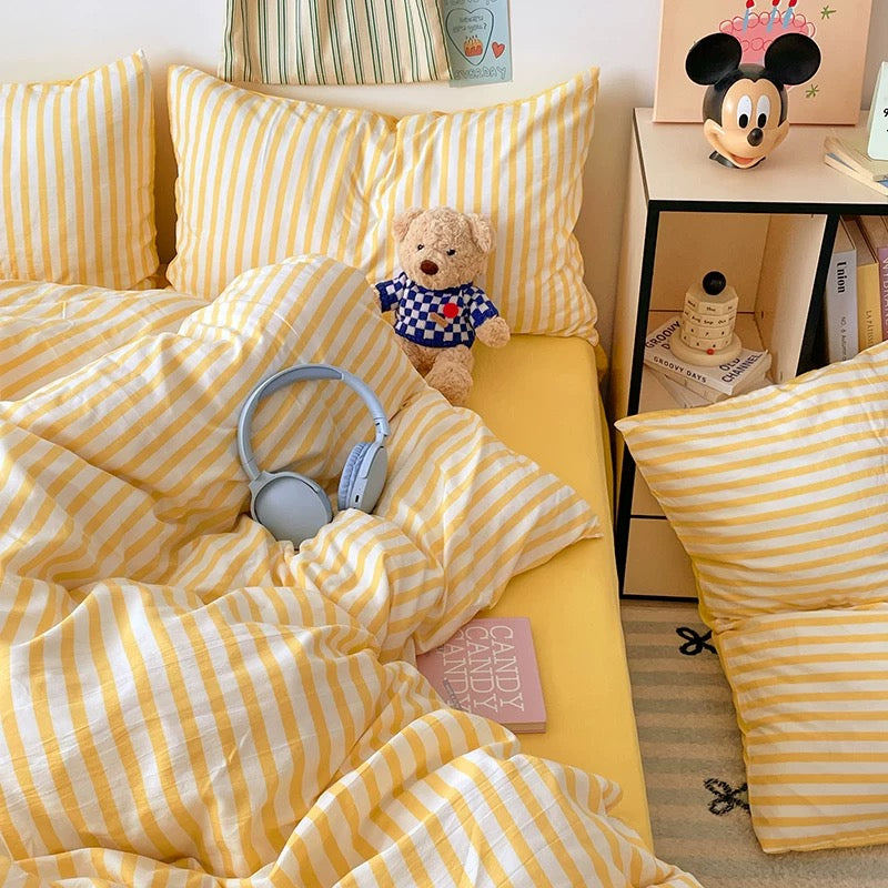 Yellow and white striped bedding with a teddy bear and headphones on a bed.