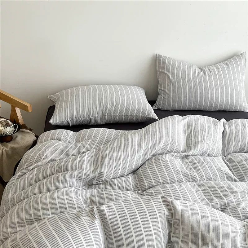 A bed dressed in a light gray and white vertically striped bedding set, including a duvet cover and two matching pillowcases, styled in a minimalist bedroom setting.