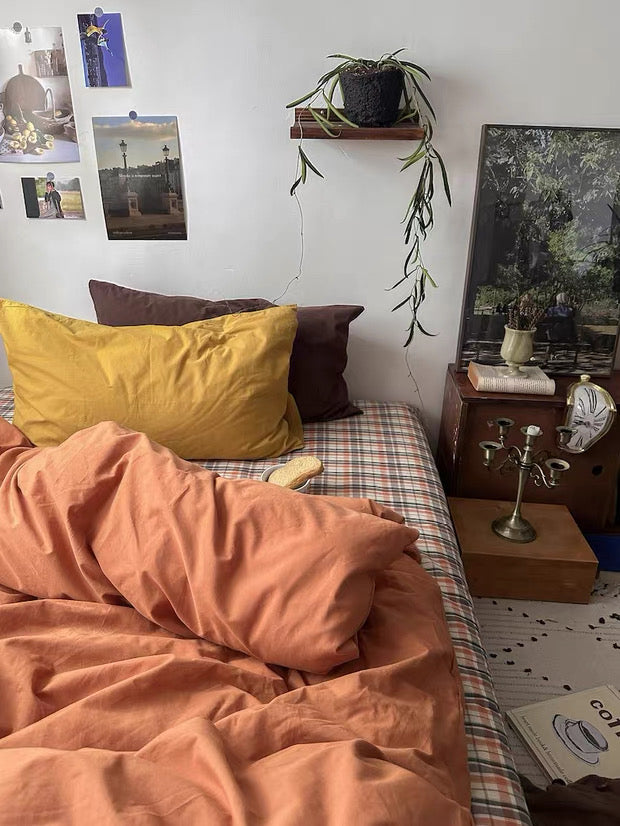 Bedroom with a bed featuring orange bedding and yellow pillow, a nightstand with a lamp, and wall decorations.