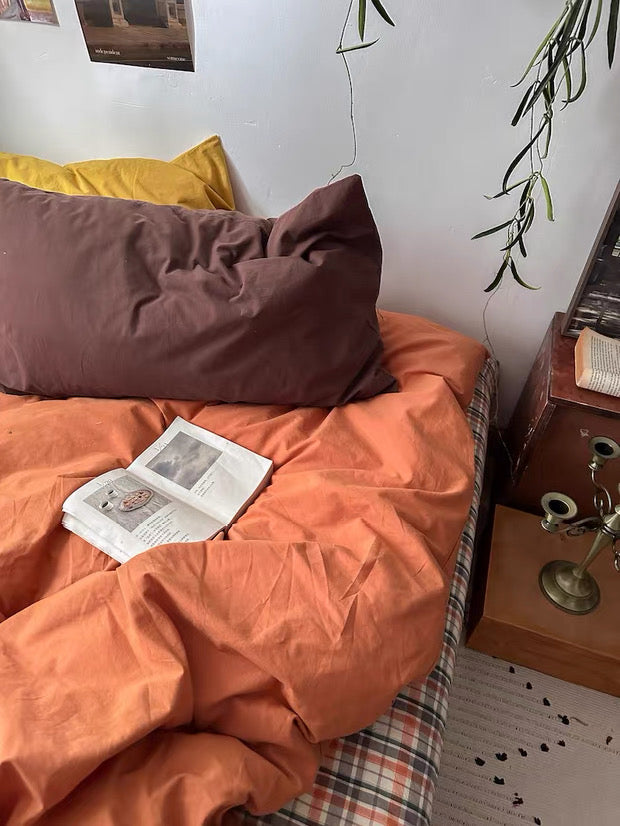 Bed with orange bedding and a book, nightstand with lamp and books in a room.