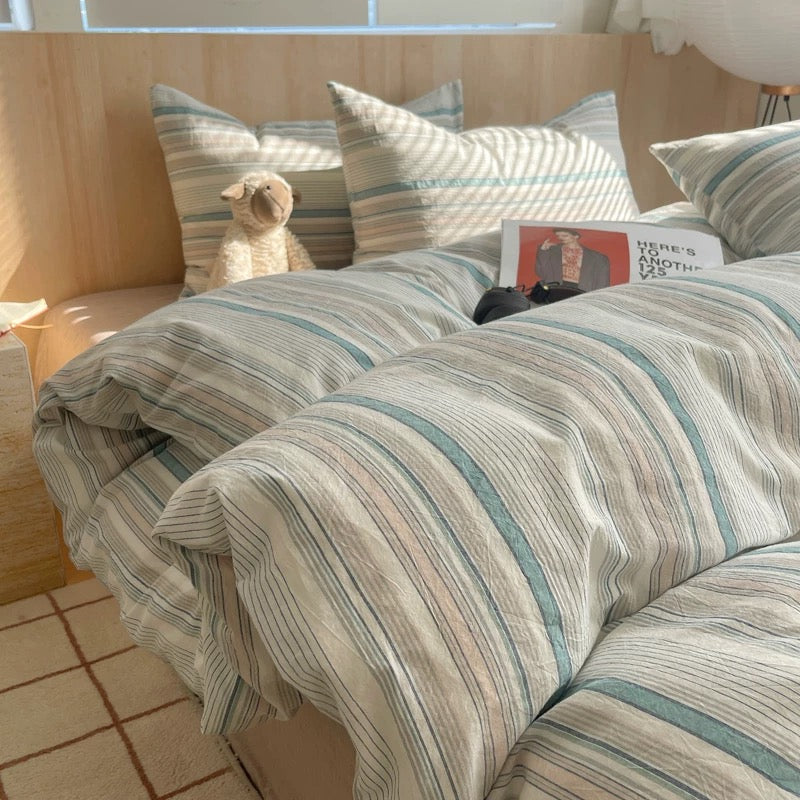 Striped duvet cover on a bed with pillows and a teddy bear in a room.
