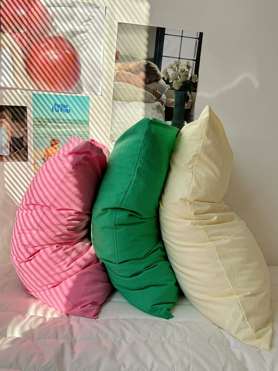 Three oversized decorative pillows in pink, green, and cream are arranged on a bed in a styled bedroom setting.