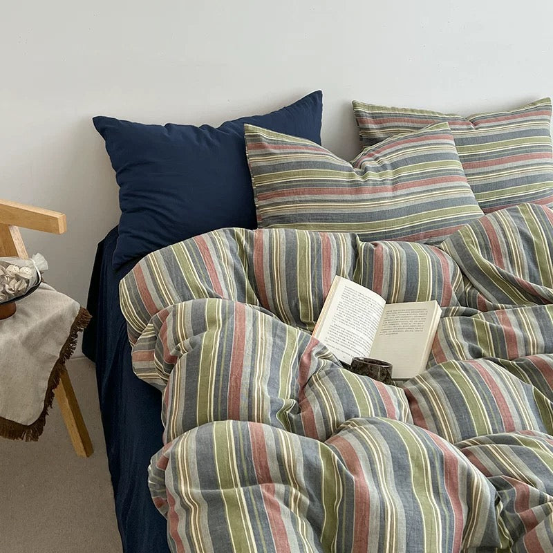 Rumpled sage and terracotta striped duvet cover piled together on a cozy unmade navy bed