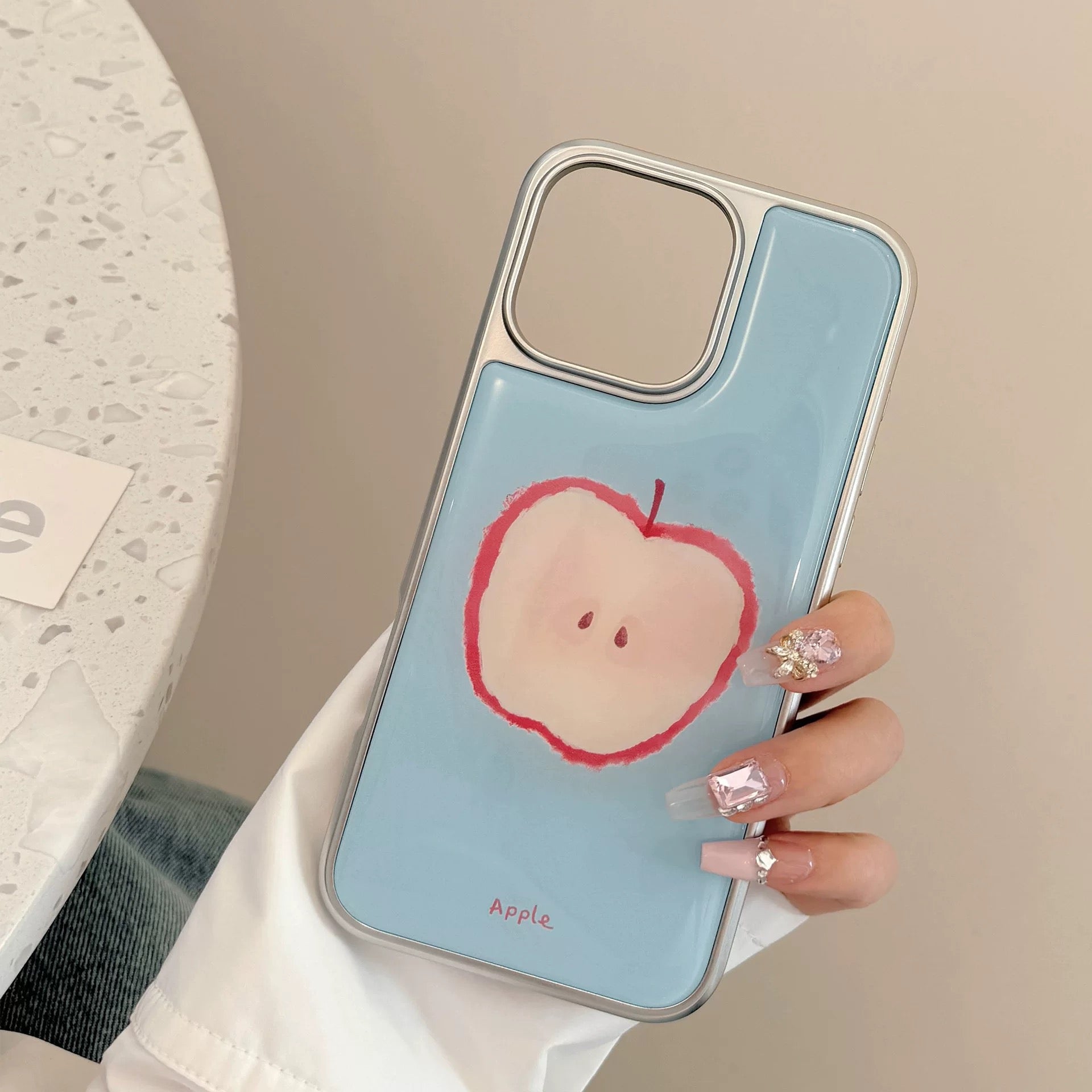 Close-up of pastel apple and guava phone cases styled on a black shelf with aesthetic accessories.
