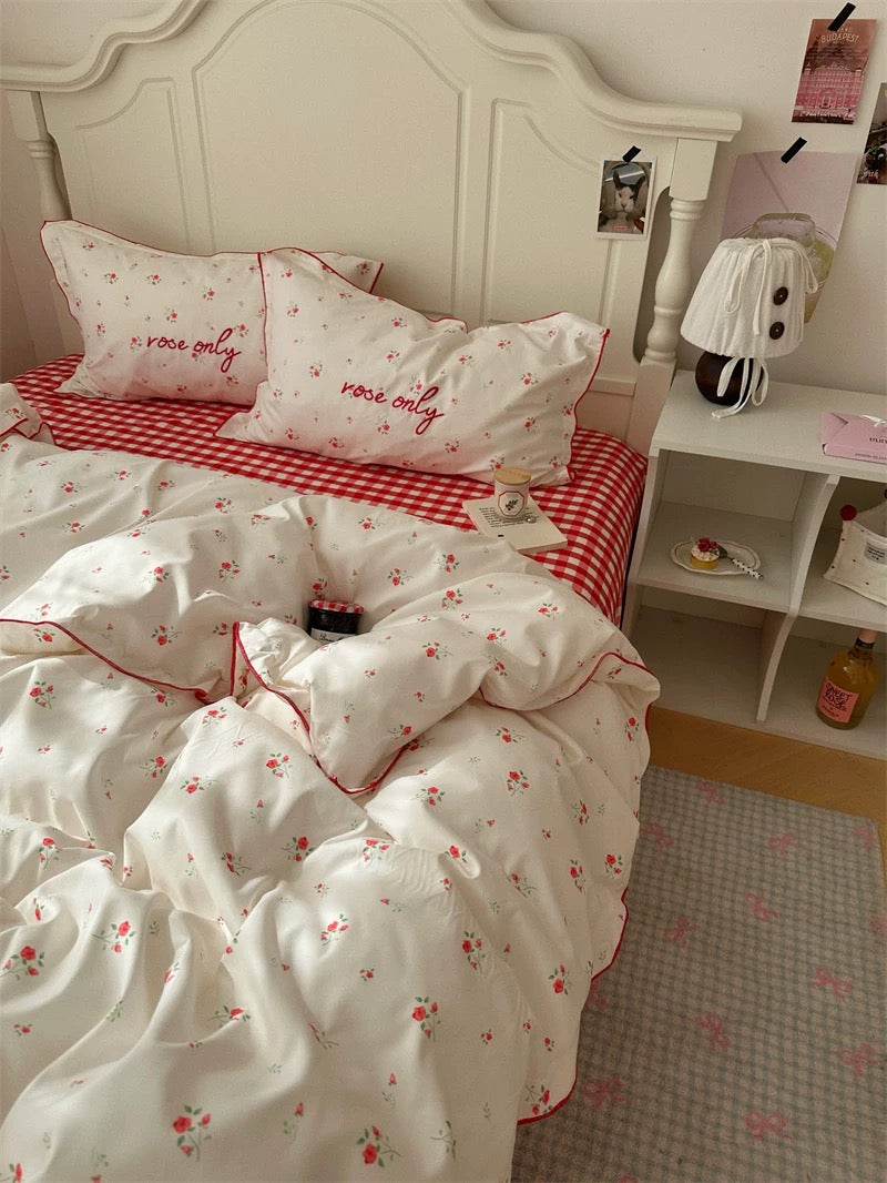 Bedroom with floral bedding and red checkered blanket, featuring 'love only' pillows.