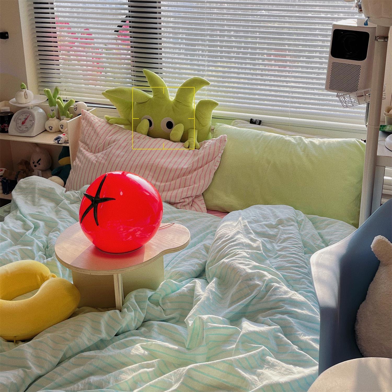 Room interior with a green couch, pink pillow, red balloon, and yellow neck pillow.