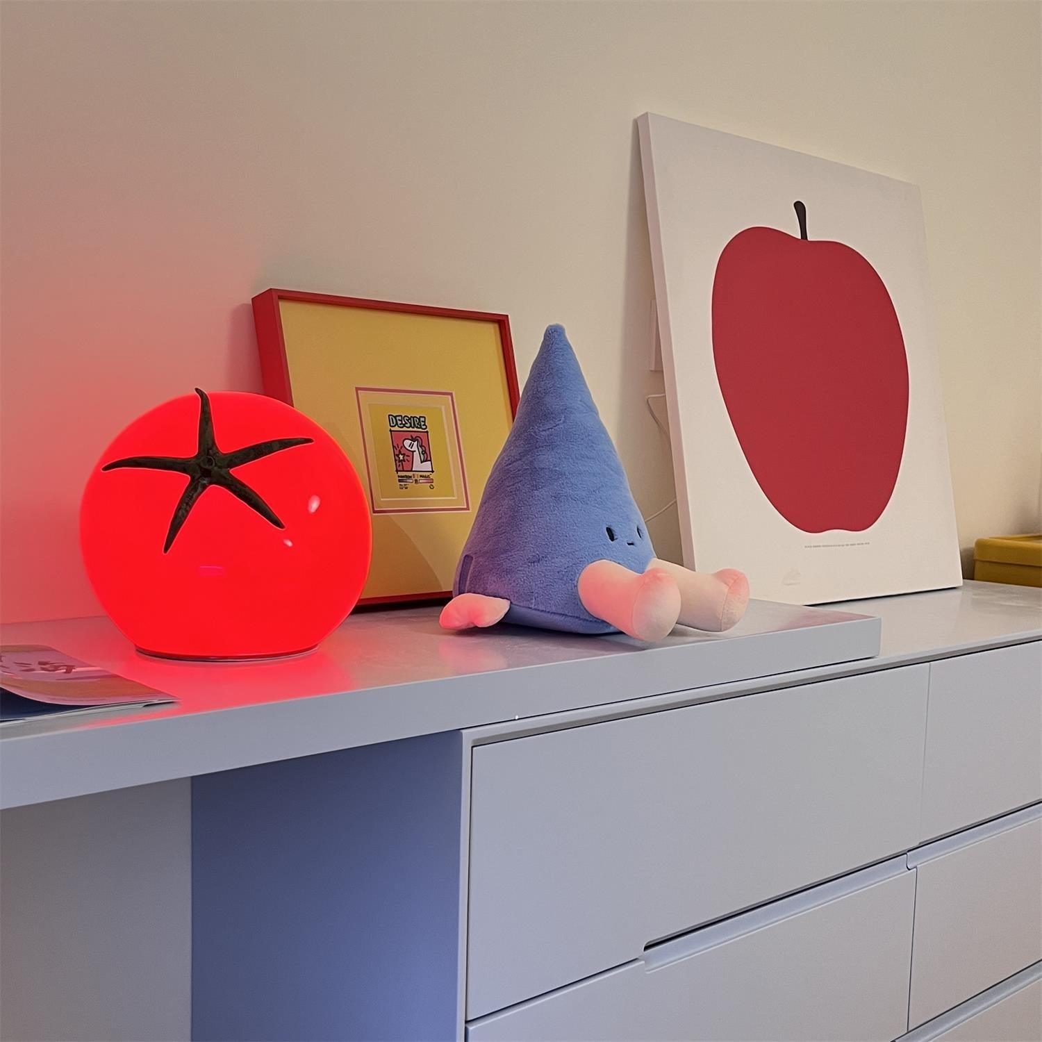 Decorative items including a red tomato-shaped lamp, blue plush toy, and framed picture of an apple on a shelf.