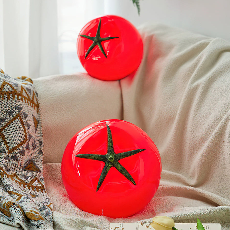 Two red tomato-shaped lamps on a couch with a blanket and tulips.