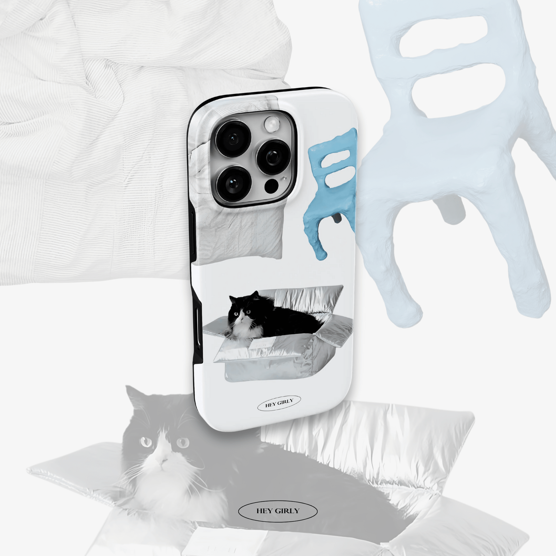 Phone case with cat design and 'Hey Girl' text, surrounded by white fabric and gloves.