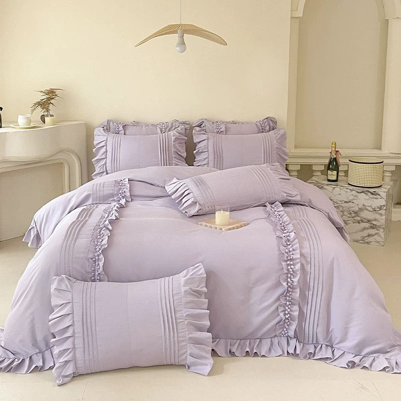 Purple bedding set with ruffled edges on a bed in a bedroom setting.