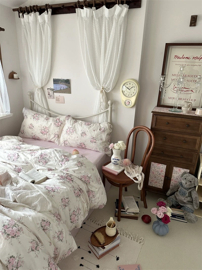 White floral bedding set featuring vintage rose print styled with wooden furniture and soft natural lighting indoors.
