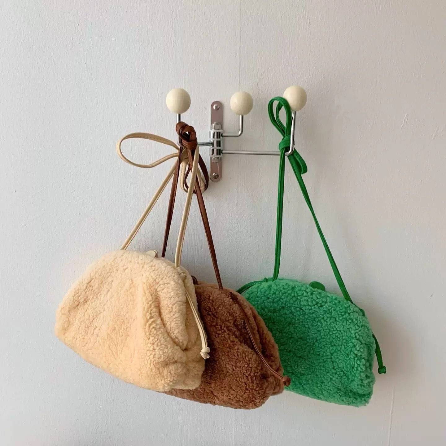 Three small bags in beige, brown, and green hanging on a wall hook.