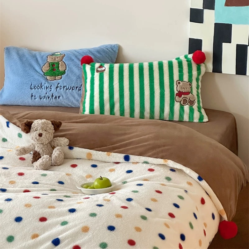 Bed with colorful polka dot blanket, teddy bear, and decorative pillows.