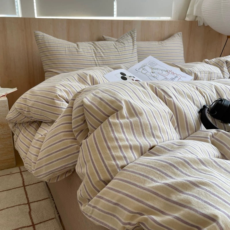 Bed with striped bedding and pillows in a room with wooden walls and a lamp.