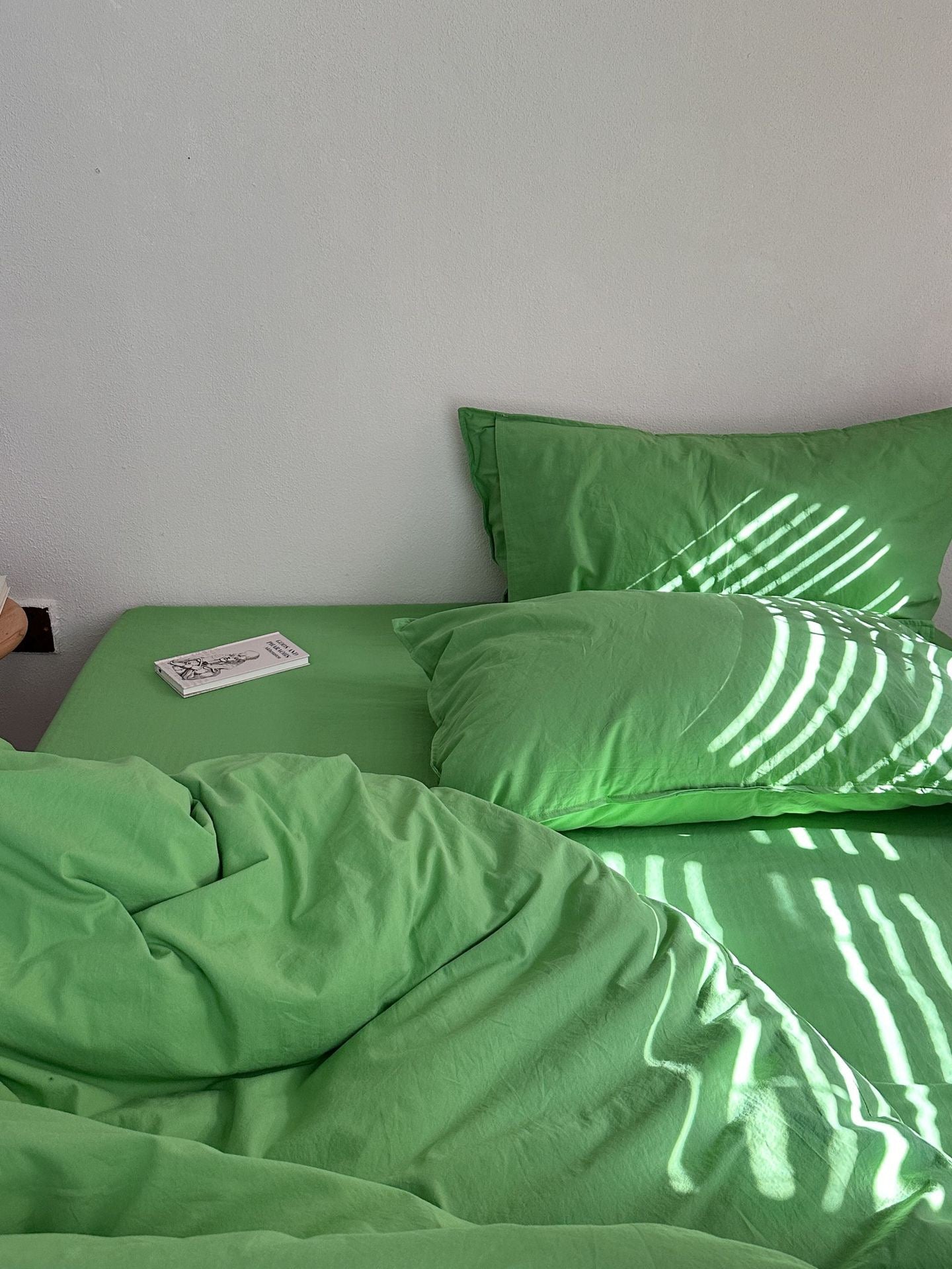 Green bedding set with matching pillowcases on a bed, featuring dappled sunlight and shadows cast across the fabric.