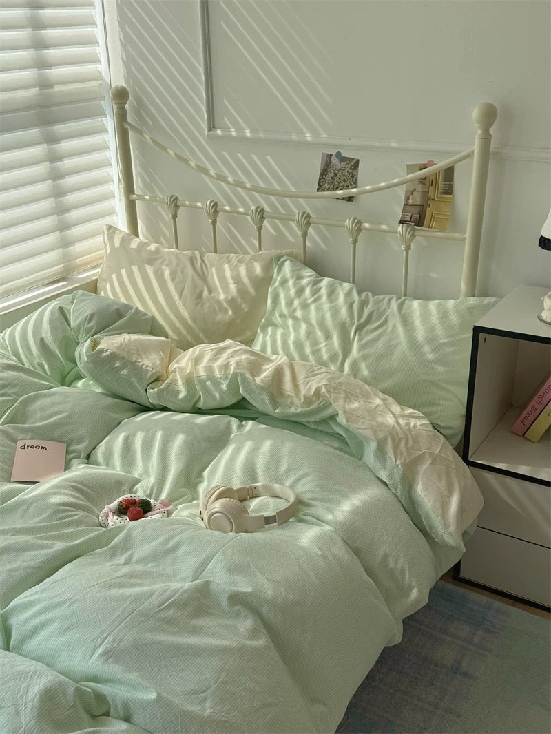 Light green bedding set on a bed with pillows and a nightstand in a room.