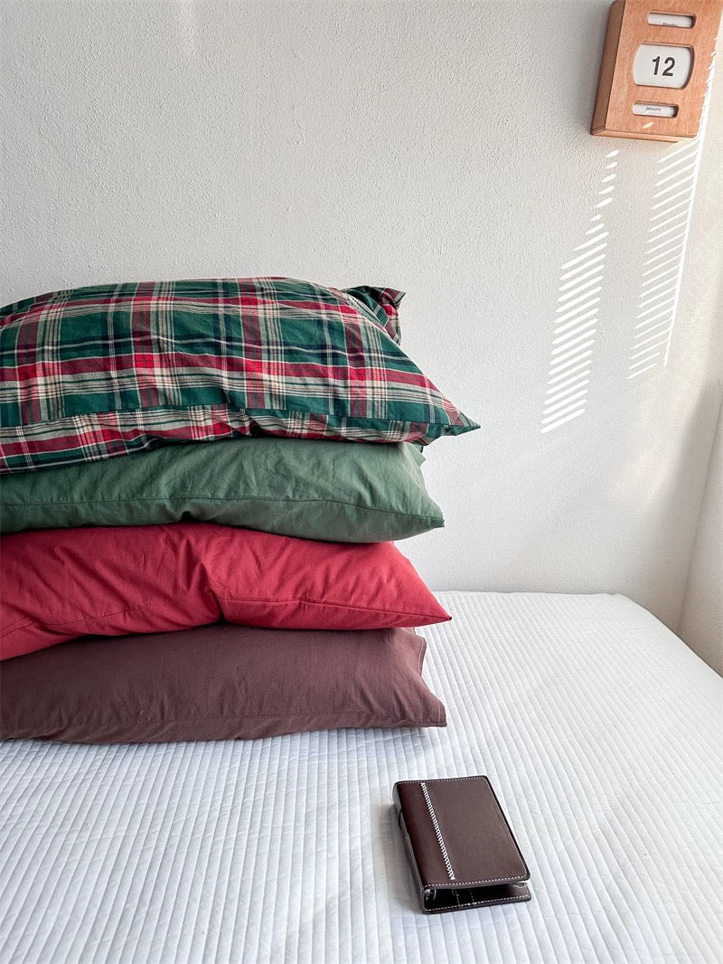 Four washed cotton pillowcase designs form a stack with tartan above green, red and chocolate brown.