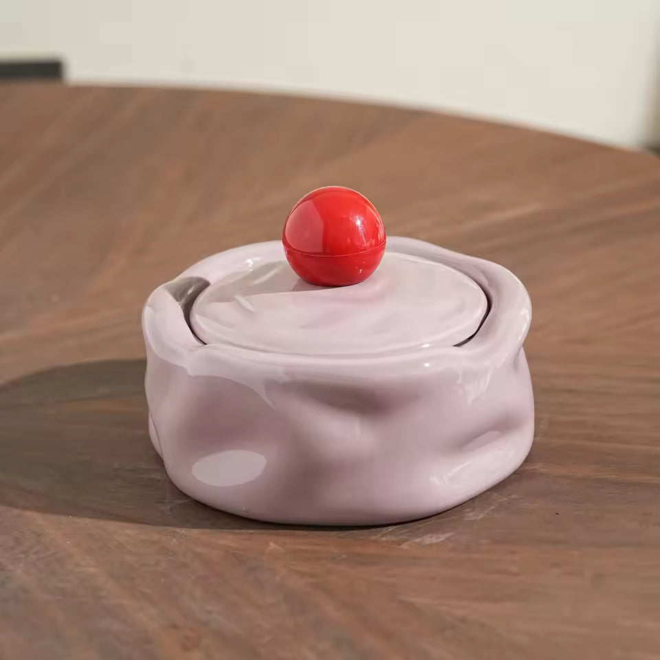 White ceramic container with a red ball on top on a wooden surface