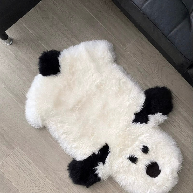 A white dog rug lies flat beside a dark sofa, with black ears and paws framing its irregular outline.