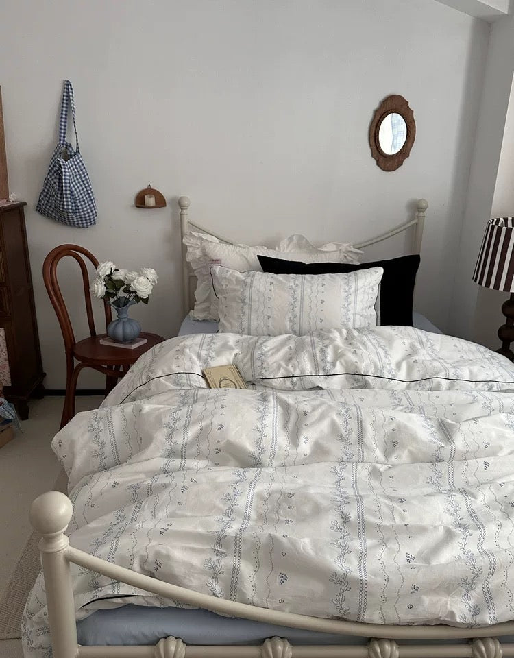 Neatly made bed in a bedroom with a chair, lamp, and window.