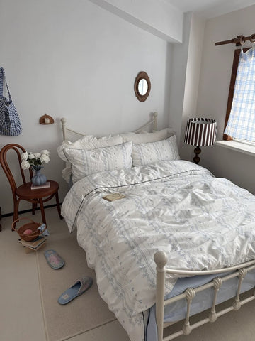 Neatly made bed in a bedroom with a chair, lamp, and window.