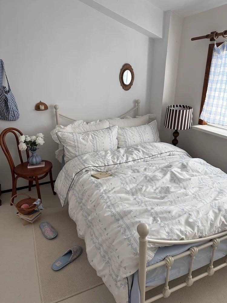 Neatly made bed in a bedroom with a chair, lamp, and window.