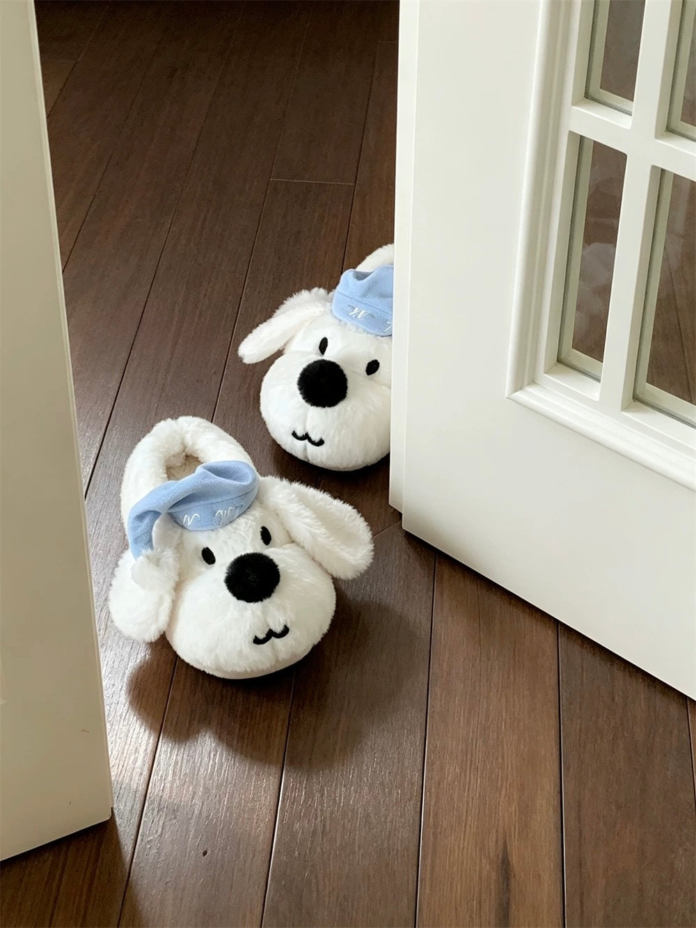 White plush dog slippers with blue sleeping caps on a wood floor