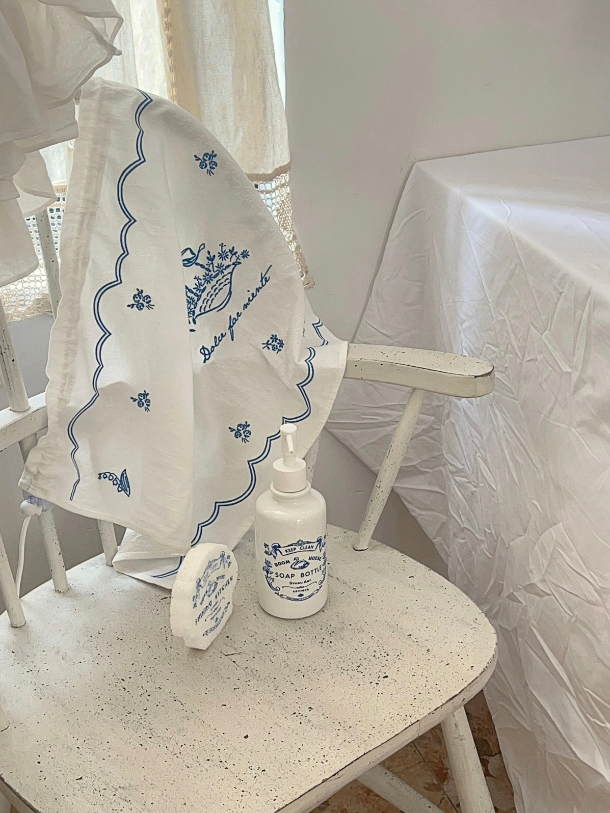 White soap dispenser sits on a round seat below draped blue fabric, with the pump turned to the side.