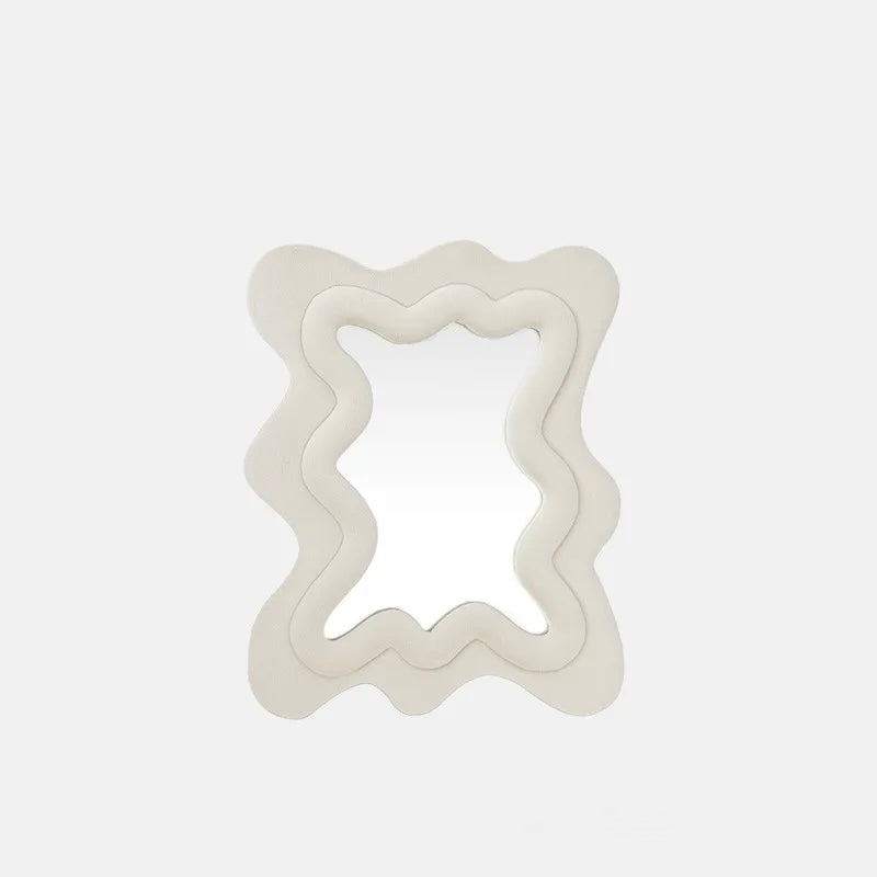 A wavy, layered mirror with a thick, sculptural frame in a matte beige finish, set against a clean, light gray background.