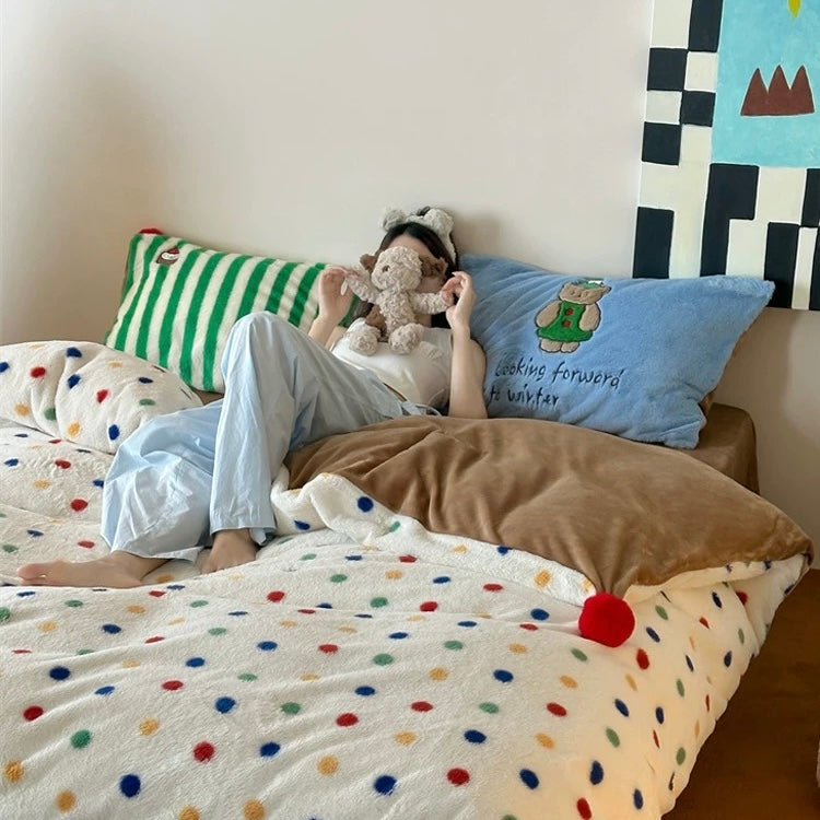 Person lying on a bed with colorful bedding and pillows, holding a teddy bear.