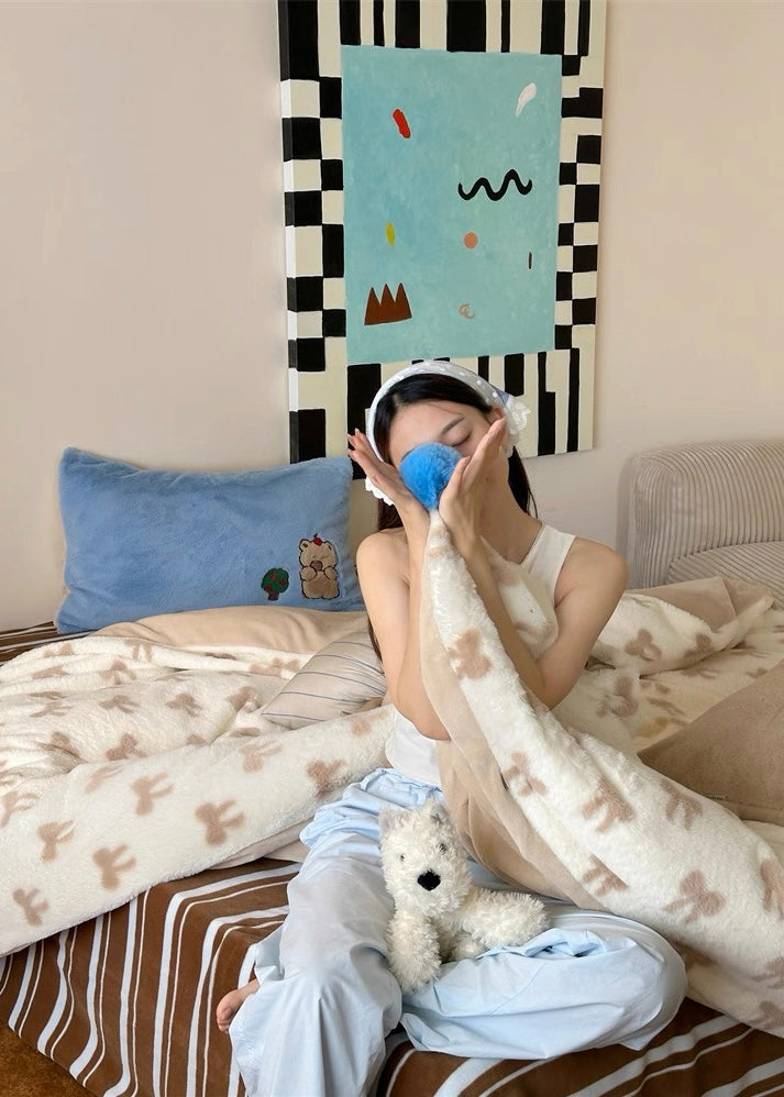 Person sitting on a bed with a blanket and pillow, holding a blue mask over their eyes.