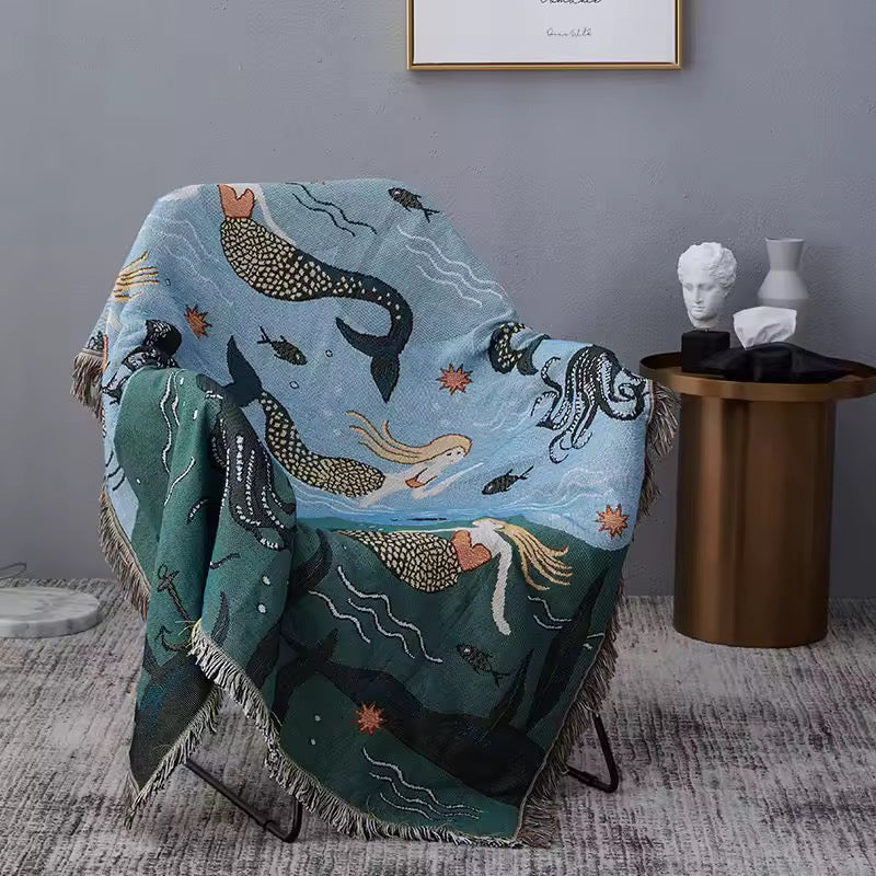 Decorative blanket with mermaid design draped over a chair in a room setting.
