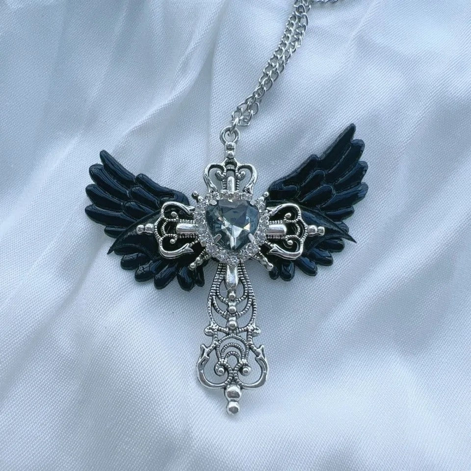 Y2K gothic necklace with angel wings and blue heart crystal. Statement jewelry with cross detail for women’s unique fashion.