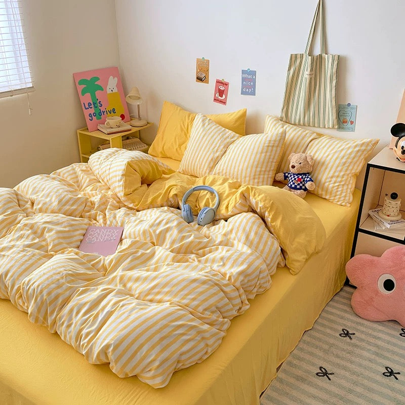 Yellow bedding set on a bed with decorative pillows and toys in a room.