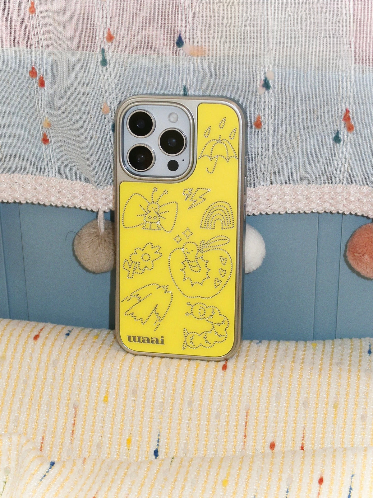 A yellow cartoon phone case standing upright, with its butterfly and apple artwork visible across the back.