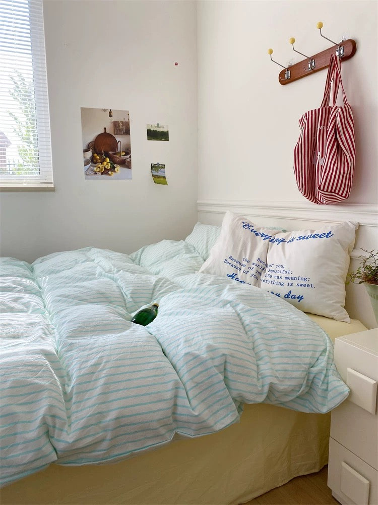 Bedroom with striped bedding, pillows, and a bag hanging on a hook.