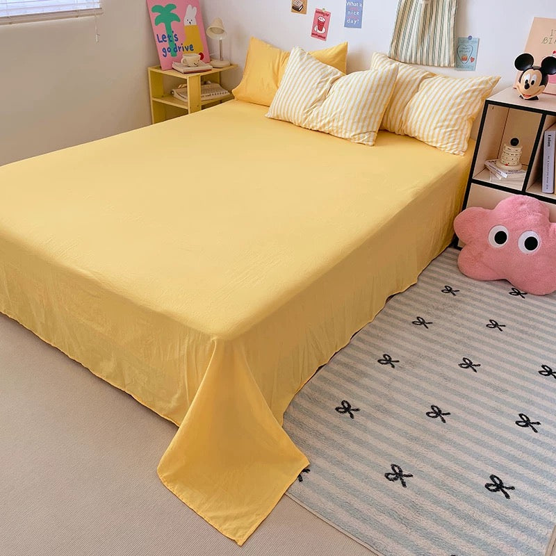 Yellow bedspread on a bed in a room with a pink pillow and decorative items.
