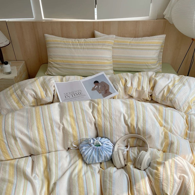 Striped bedding with a book, hot water bottle, and headphones on a bed.