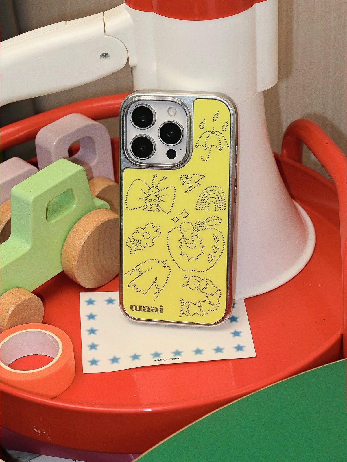 A yellow Y2K phone case in a closer upright view, showing the silver outlines and camera opening.